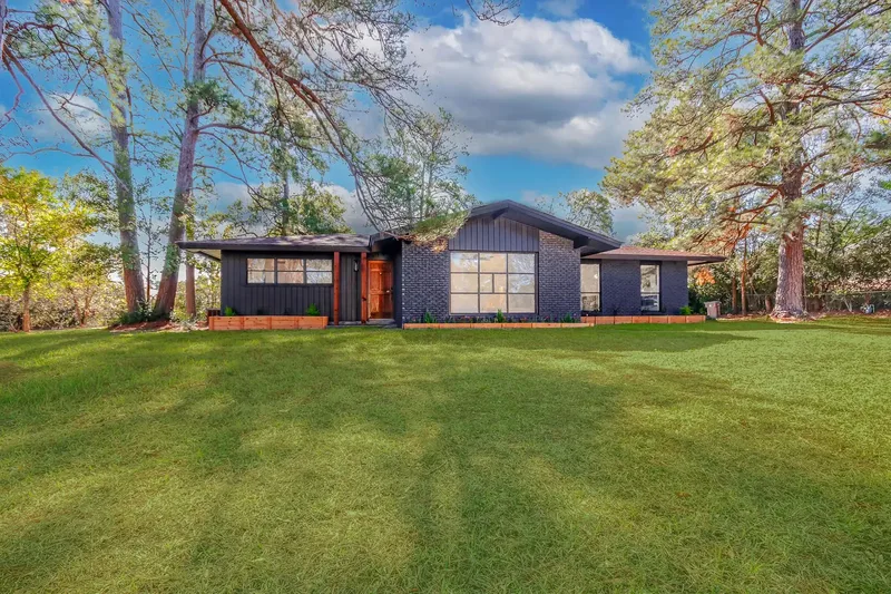 A finished custom home by Green and Co., dark board-and-batten and brick exterior framed by tall pines