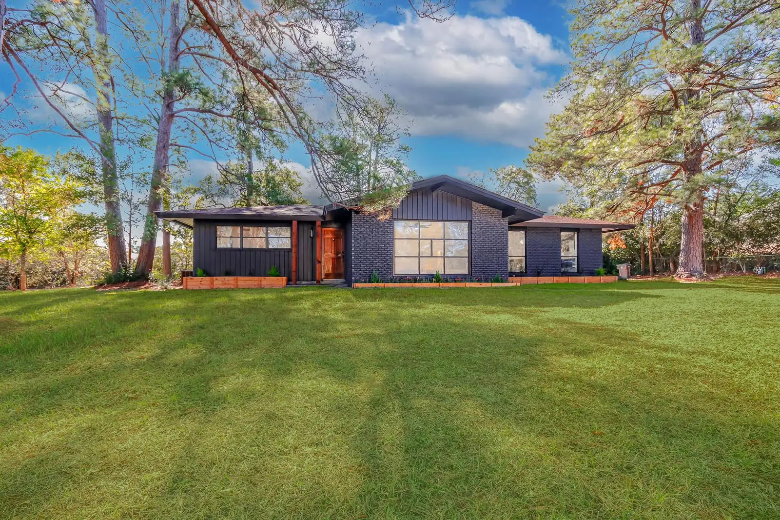 A finished custom home by Green and Co., dark board-and-batten and brick exterior framed by tall pines