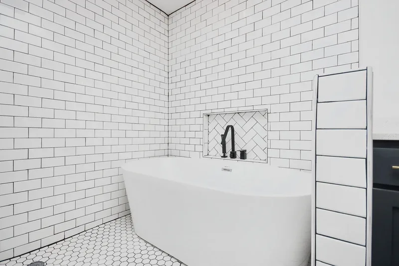 The finished tub area: freestanding soaking tub, white subway tile, a herringbone niche, and a hexagon tile floor with a central drain