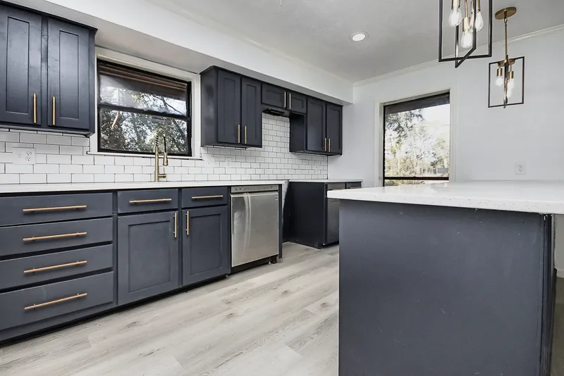 Finished navy cabinet run with gold pulls, subway tile backsplash, and a stainless dishwasher beside the island