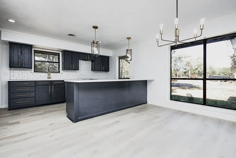 The finished kitchen remodel: navy cabinetry, gold pendants, white subway tile, and a long island open to the dining area
