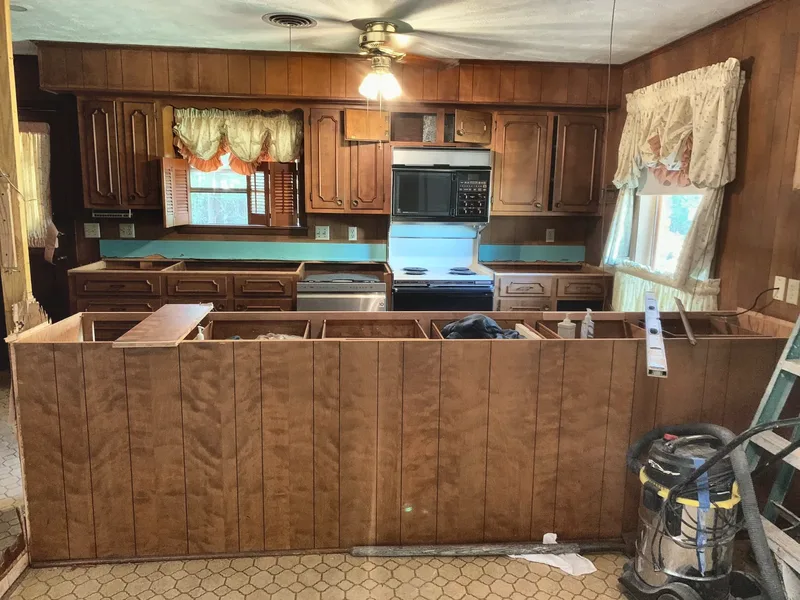 The original kitchen before remodeling, with dark wood cabinetry, dated laminate counters, and a closed-in peninsula