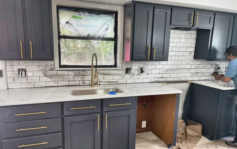 The sink wall during install, with new counters, a gold faucet, gold cabinet pulls, and subway tile going up