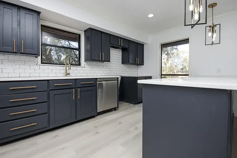 Navy shaker kitchen cabinets with gold pulls, subway backsplash, and stainless appliances